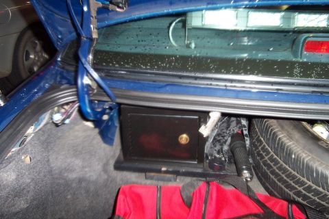1998 Ford Crown Victoria - Open trunk of a blue sedan showing gray carpeted cargo area with a small black lock box or safe bolted to the floor, a spare tire lying on…