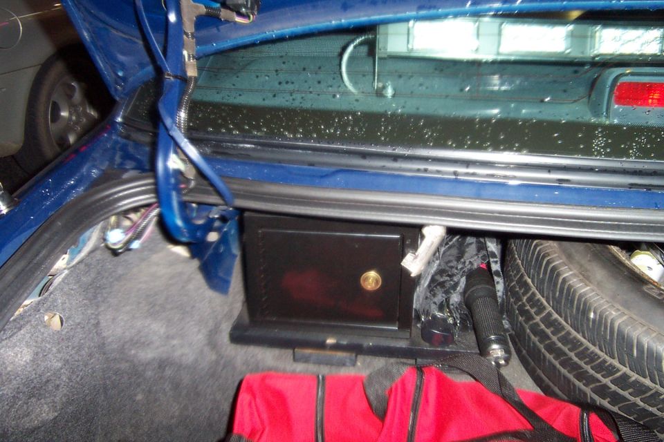 Blue sedan trunk with black lock box, spare tire, flashlight and red duffel bag