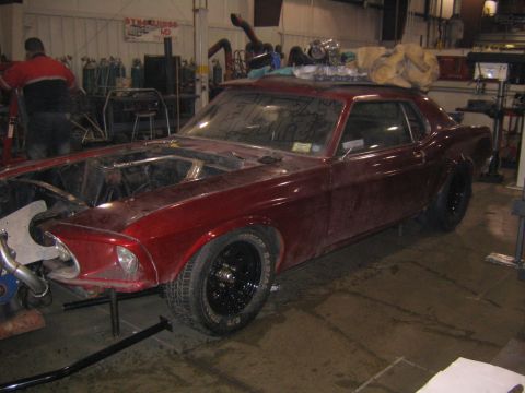 1969 Ford Mustang - This 1969 Ford Mustang is undergoing work in a garage, with its hood up and engine exposed.