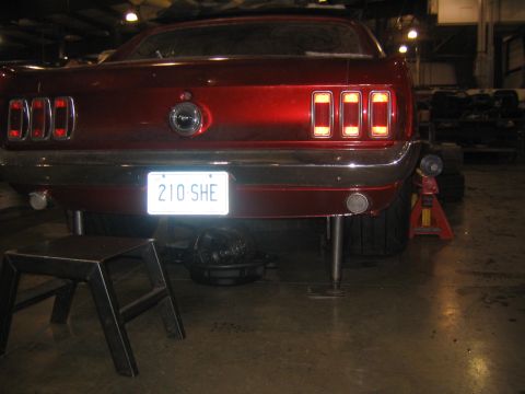 1969 Ford Mustang - The rear of a classic red Mustang is shown elevated on jack stands in a workshop setting.