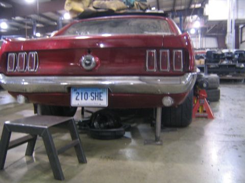 1969 Ford Mustang - The rear of a red 1969 Ford Mustang is visible, raised on jack stands in a workshop setting.