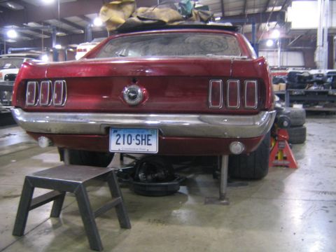 1969 Ford Mustang - Rear view of a red 1969 Ford Mustang, triple taillights and a chrome bumper, supported by jack stands.