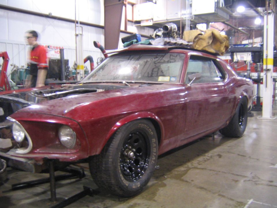 1969 Ford Mustang with hood removed, sitting on jack stands in a garage