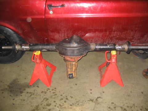 1969 Ford Mustang - A rear axle assembly is supported by red jack stands, with the side of a red vehicle visible in the background.