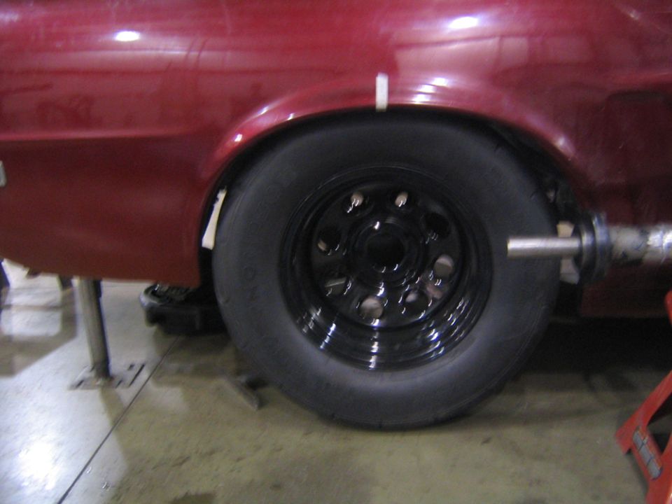 Red car's rear wheel well with a black rim and tire, under a lift