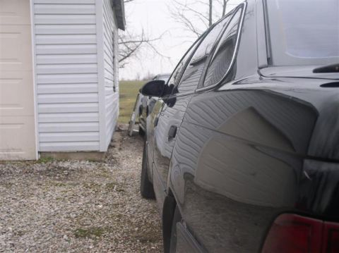 1997 Ford Taurus - A black sedan is parked beside a white building, with another vehicle visible in the background.