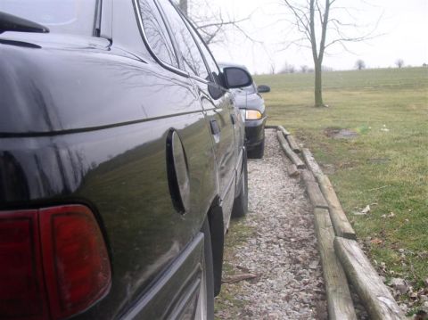 1997 Ford Taurus - Two cars are parked side-by-side on a gravel area next to a grassy field.