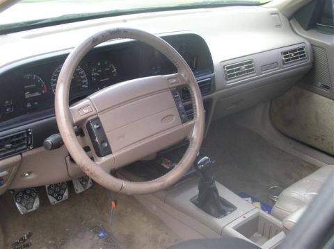 1997 Ford Taurus - The interior of a 1997 Ford Taurus shows a tan dashboard, worn steering wheel, and a manual transmission shifter.
