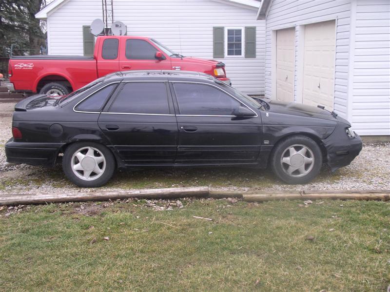 Side view of a black sedan parked next to a red pickup truck in a driveway
