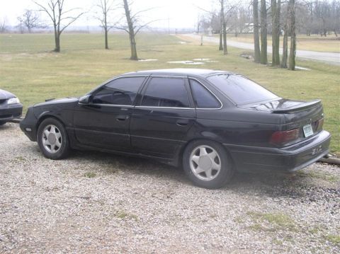 1997 Ford Taurus - A black sedan is parked on a gravel lot with trees in the background.