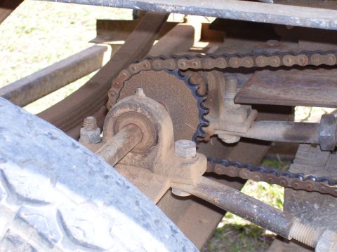 1992 Ford Bronco - A close-up view of a rusty chain and sprocket assembly, part of a vehicle's drivetrain, with a tire visible.