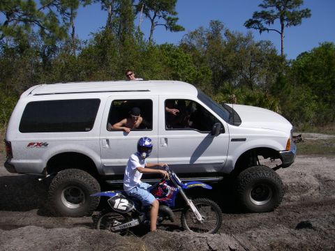 2000 Ford Excursion - A lifted 2000 Ford Excursion is parked off-road with several people inside and a dirt bike positioned in front of it.