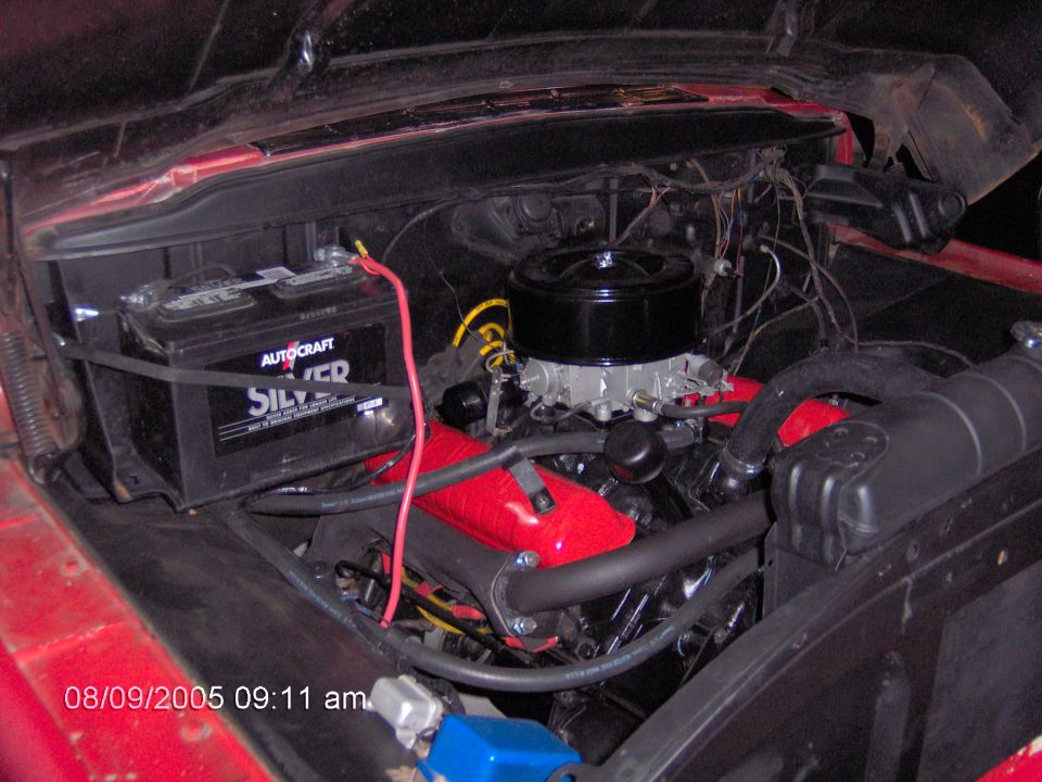 Red engine bay with black air cleaner, red valve covers, and Autocraft battery. Visible radiator and hoses