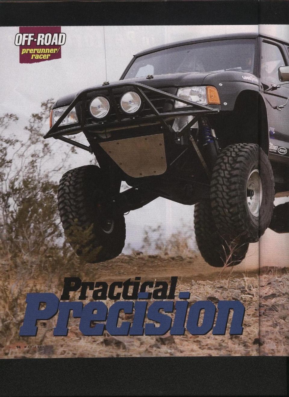 Black off-road prerunner truck mid-air, custom front bumper, large tires, desert terrain