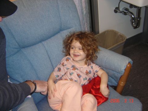 1993 Ford Bronco - A young child with curly red hair smiles while sitting in a blue armchair, with a sink and trash can visible in the background.