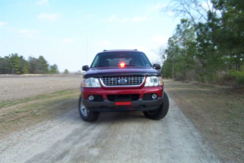 2005 Ford Explorer - Front view of a red 2005 Ford Explorer parked on a dirt road with trees in the background.