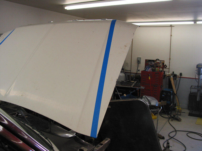 White truck hood propped open with blue tape guide stripes in a home shop