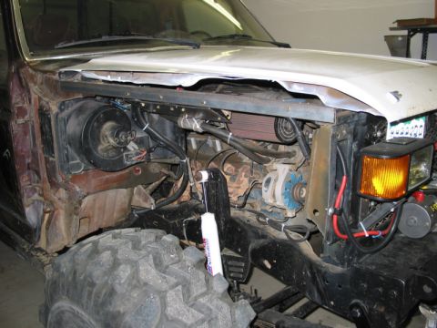 1981 Ford Bronco - The engine bay of a modified off-road vehicle is visible, with a large tire in the foreground and various mechanical components exposed.