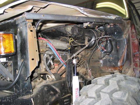 1981 Ford Bronco - The engine bay of a 1981 Ford Bronco shows exposed mechanical components and wiring, with a large off-road tire visible.