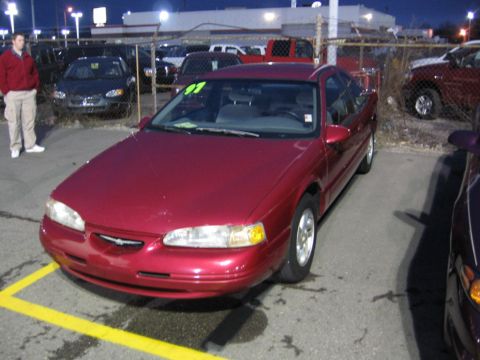 1995 Ford Thunderbird - A red 1995 Ford Thunderbird is parked in a lot with other vehicles visible.