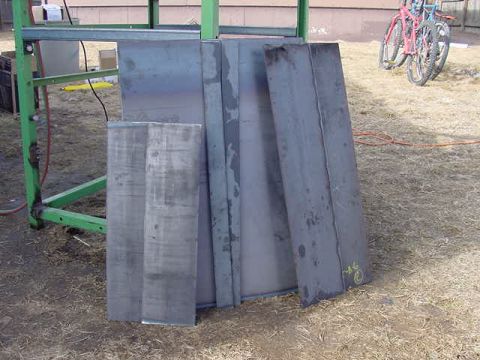 1981 Ford Bronco - Metal plates are stacked and leaning against a green metal structure on a dry, grassy surface.