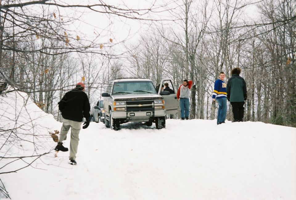 Silver Chevrolet pickup truck with open driver door, people standing around in snow. Another vehicle behind it