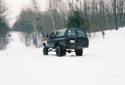 2000 Chevrolet Tahoe - A lifted SUV drives through a snowy landscape with trees on either side of the road.