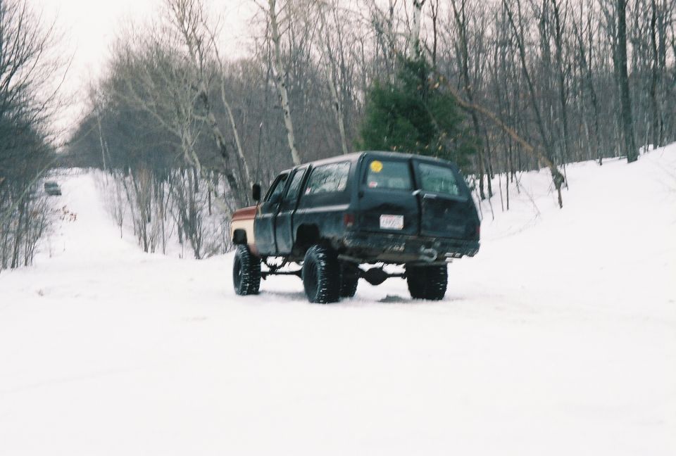 Lifted black and brown SUV on a snowy hill, rear view. It has large tires and a tow hitch