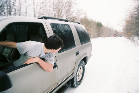 2000 Chevrolet Tahoe - A man leans out the window of a beige SUV as it drives down a snow-covered road, with another vehicle visible in the distance.