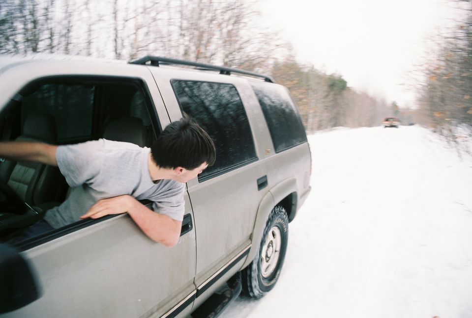 Side view of a beige 1990s SUV with a man leaning out the window, driving on a snowy road