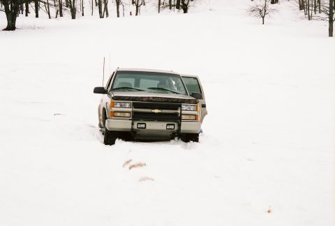 2000 Chevrolet Tahoe - Silver Chevrolet Tahoe with open driver's door stuck in deep snow, front view.