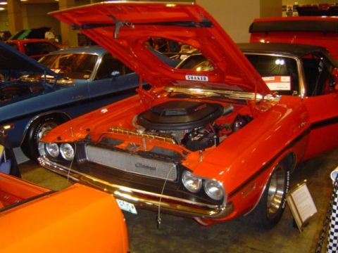 1979 Ford Bronco - Orange muscle car on display with hood open, showing engine details. Another car is parked behind it.