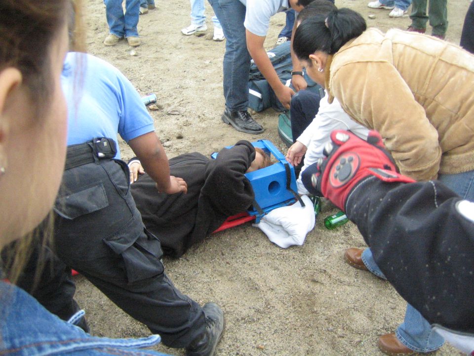 Injured person on ground in blue head immobilizer as medics and bystanders kneel on sand