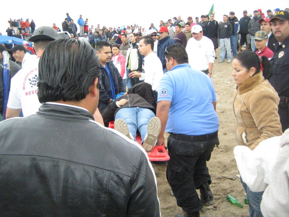 Rescue crew carrying a person on a red backboard stretcher through a crowd outdoors