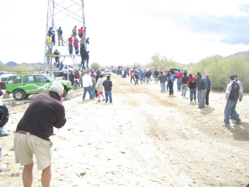 Man photographing a sandy desert trail crowded with spectators and a scaffold tower