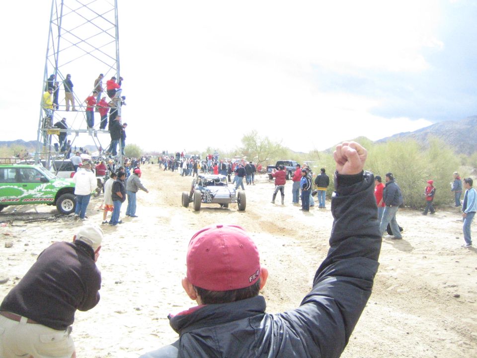 Spectator raises a fist as an off-road buggy drives a sandy desert trail