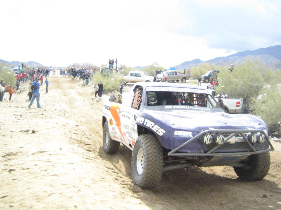 Purple trophy truck with KC lights and BFGoodrich decals on sandy desert track