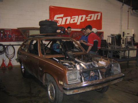 1978 Ford Bronco - A modified brown hatchback sits in a garage with its engine exposed and a roll cage visible inside.