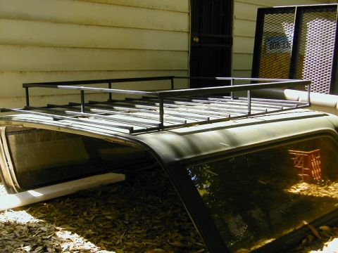 1993 Ford Bronco - A black steel roof rack with tubular railings and slatted floor mounted on the roof of a dark green SUV, photographed from above and behind…