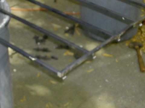 1993 Ford Bronco - Blurry close-up of a shop-fabricated rack or grate welded from square steel tubing, resting over a concrete floor with an orange extension…
