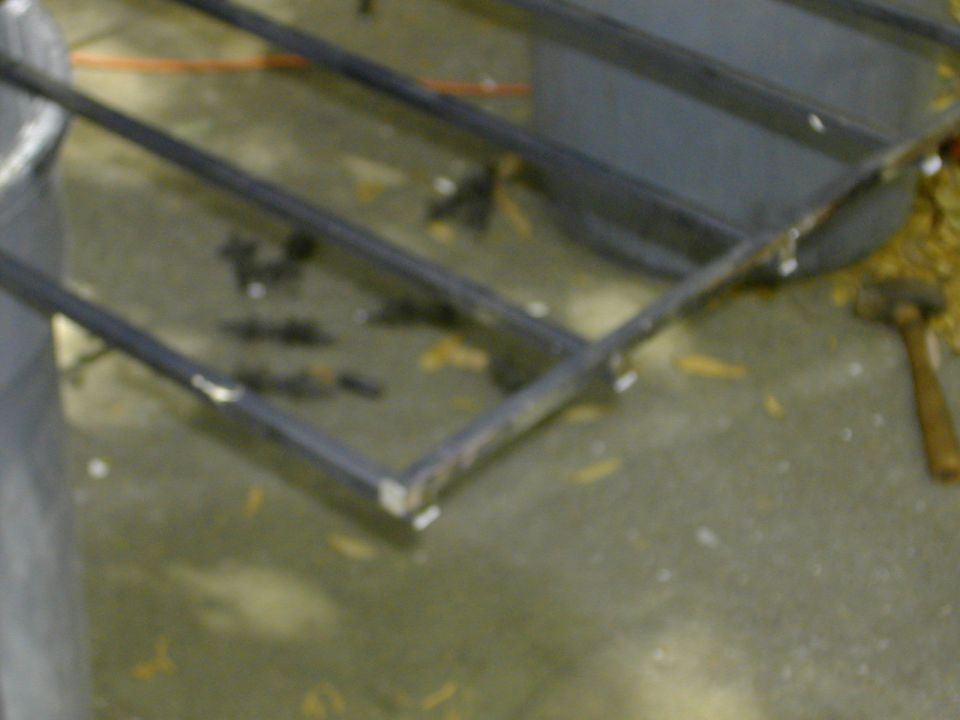 Close-up of welded square steel tube frame on concrete shop floor with hammer nearby