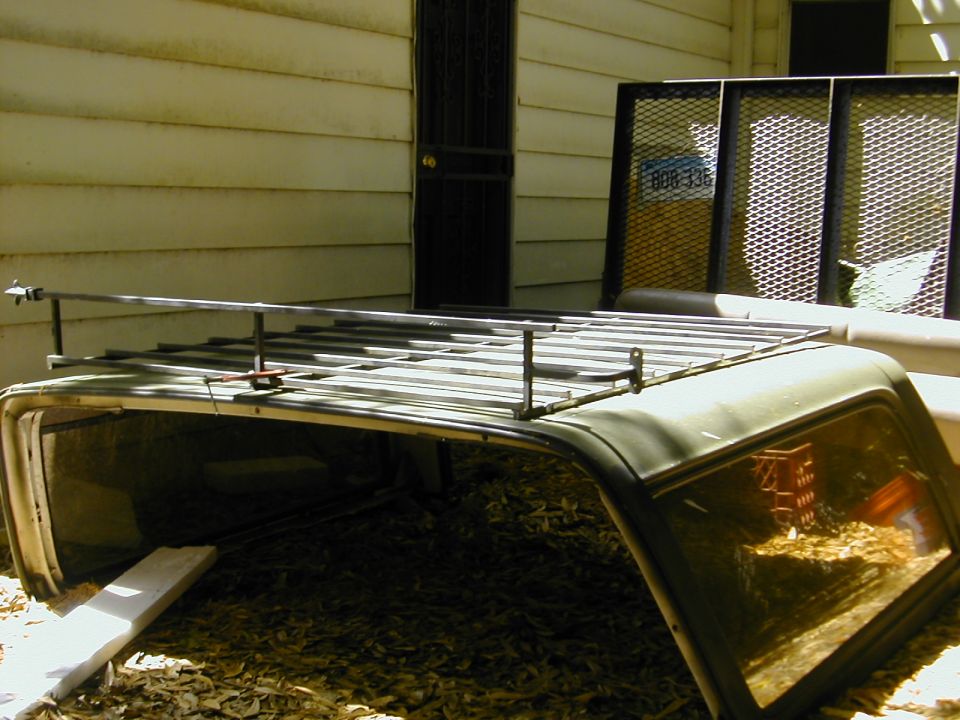 Removed SUV hardtop on ground with bare steel roof rack test-fitted