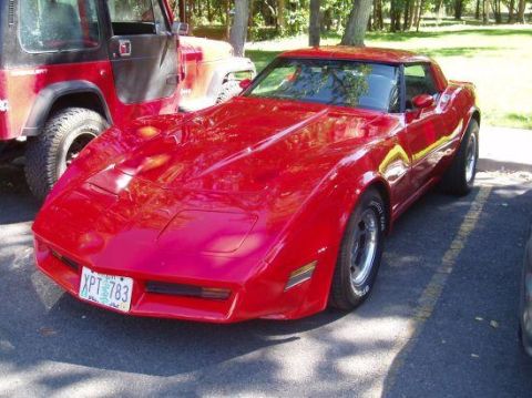 1982 Chevrolet Corvette - A red Chevrolet Corvette is parked in a lot next to a red Jeep.