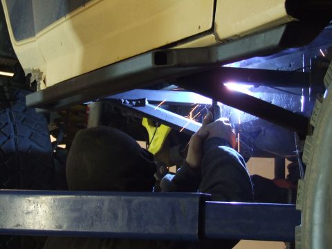 1986 Ford Bronco - Custom rock sliders are being welded onto the frame of a vehicle.