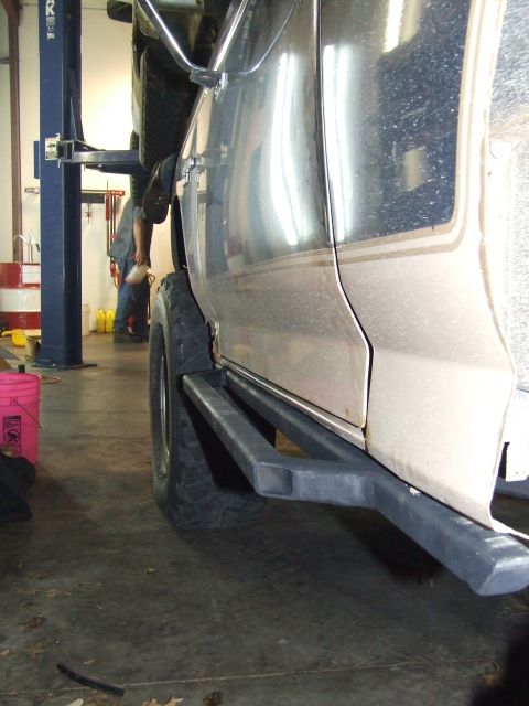 1986 Ford Bronco - Aftermarket rock sliders are visible on the side of a vehicle being worked on in a garage.