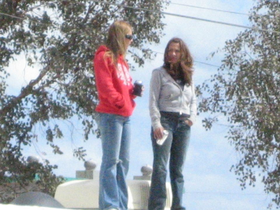 Two young women standing on a light-colored vehicle roof among bare trees