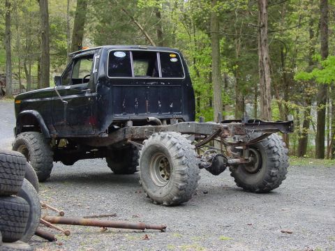 1984 Ford F-250 - This modified pickup truck chassis sits on large off-road tires, with its bed removed and frame exposed.