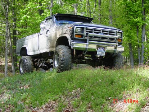 1984 Ford F-250 - Mud-splattered Ford pickup truck with large tires sits on a grassy hill surrounded by trees.