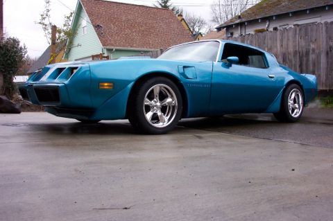 1979 Pontiac Trans Am - A blue 1979 Pontiac Trans Am is parked on a wet concrete surface, its distinctive body style and chrome wheels.