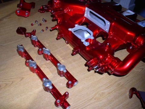 1996 Ford Probe - Engine intake manifold and fuel rails, freshly painted in a metallic red finish, are laid out on a wooden surface.